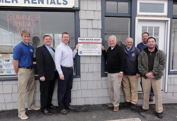  Officials at the unveiling of a high mark mark sign at Wood Agency in Manasquan. Pictured (l to r): Christopher Huch, Community Resiliency Specialist from the Jacques Cousteau Research Reserve; Owen McCarthy, Councilman & Chair of the Public Safety Committee; Ray Krudzlo, Senior Service Hydrologist, National Weather Service Forecast Office Mount Holly; Robert Wood, Owner, Wood Agency; George Dempsey, Mayor; Joseph Bossone, Concilman & OEM Liaison; and Joseph Miketta, Warning Coordination Meteorologist, National Weather Service Forecast Office Mount Holly. (Photo courtesy of the Manasquan Office of Emergency Management) 