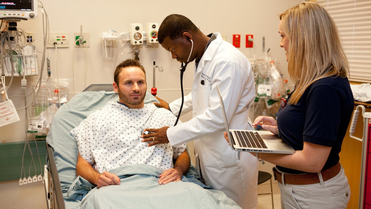 A scribe enters patient data into a laptop while a doctor performs an examination. (Image courtesy of Scribe America)