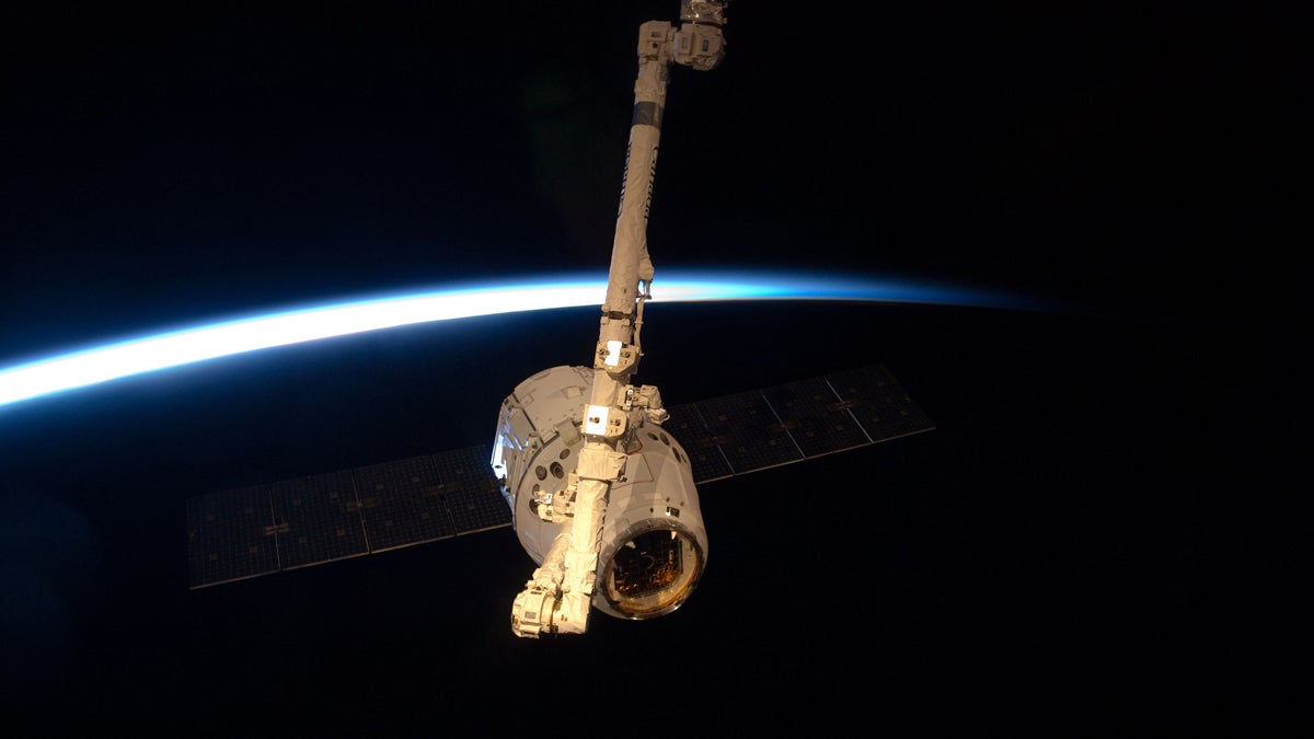  SpaceX Dragon berths at the International Space Station.  With darkness, Earth's horizon and thin line of atmosphere forming a backdrop, the SpaceX Dragon commercial cargo craft is grappled by the Canadarm2 robotic arm at the International Space Station. (Image courtesy of NASA/JSC) 