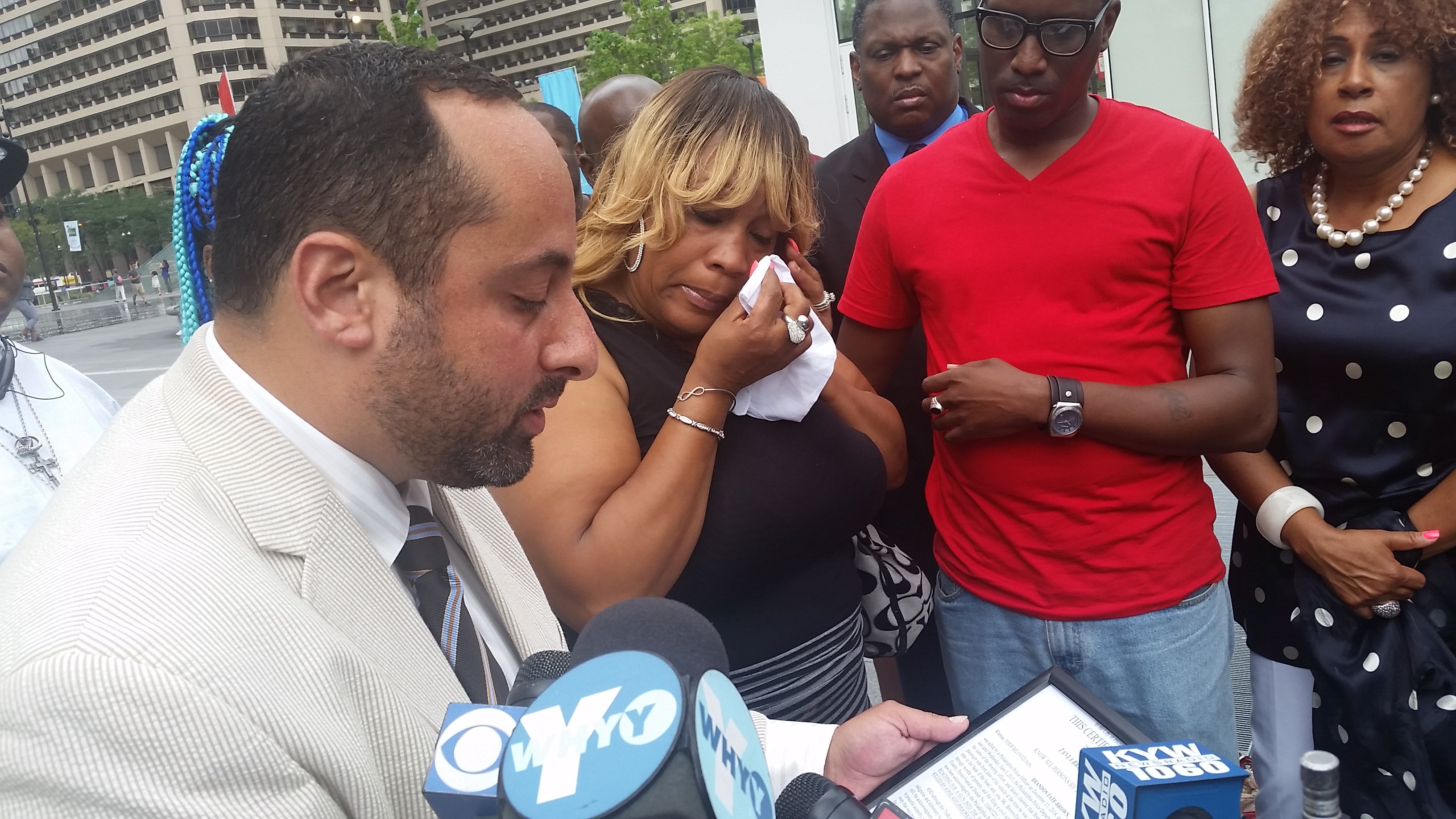  As family attorney Brian Mildenbergspeaks, Brandon Tate-Brown's mother wipes tears from her eyes at a City Hall press conference. (Tom MacDonald/WHYY)  