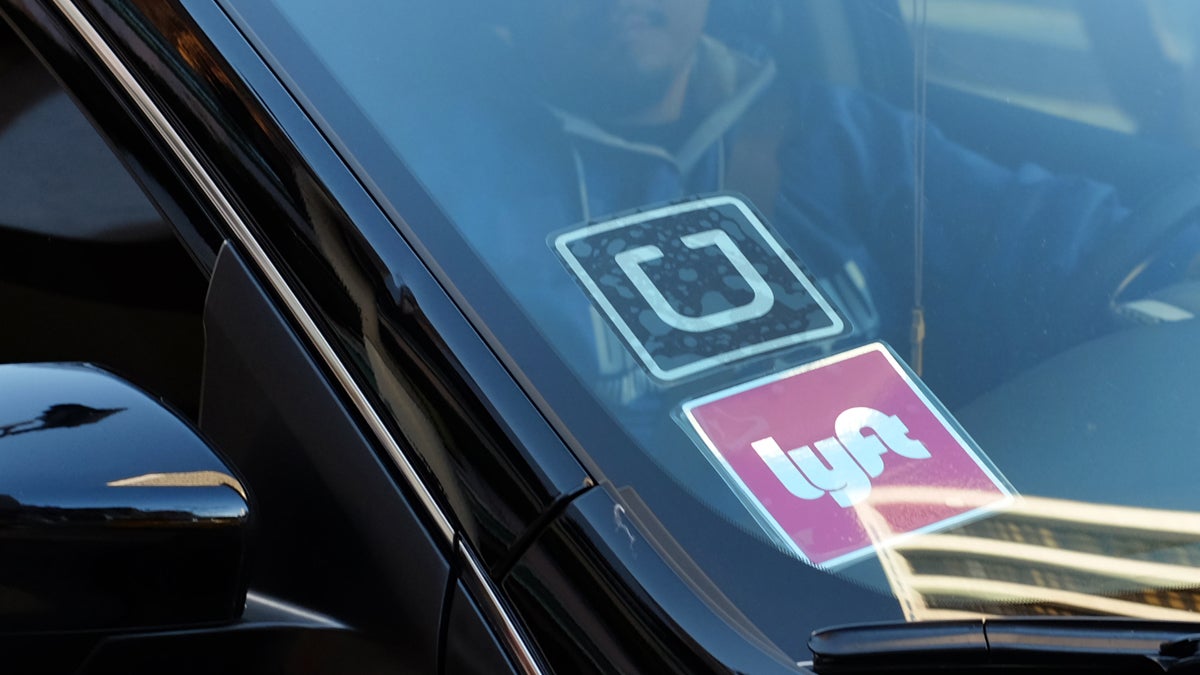 A driver displaying Lyft and Uber stickers on his front windshield is shown dropping off a customer in downtown Los Angeles. (AP Photo/Richard Vogel