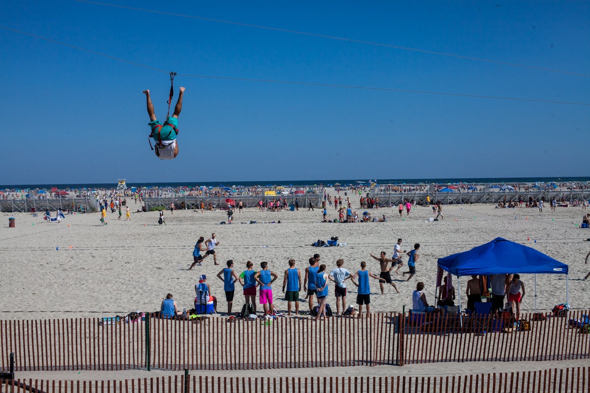 A man goes down a zipline while games of ultimate frisbee are played on the beach in WIldwood, Nj. (Brad Larrison/for NewsWorks)