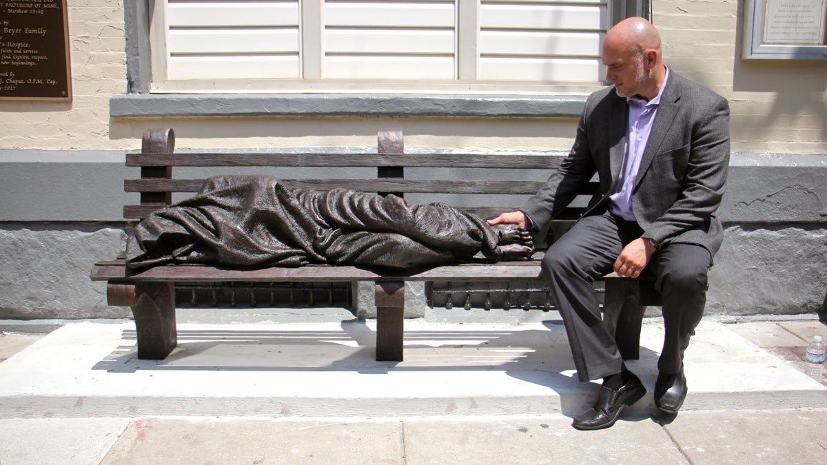 Artist Timothy Schmalz sits beside his sculpture, ''Homeless Jesus,'' outside St. John's Hospice on Race Street. (Emma Lee/WHYY)