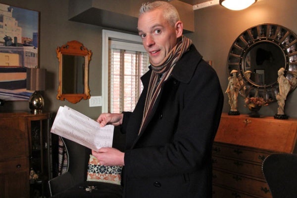 <p>Will Massey, standing in the living room of his Carpenter Street home, holds a list he compiled of 400 properties that have sold in the last year. The city's assessment of their value, he says, are way off. (Emma Lee/for NewsWorks)</p>

