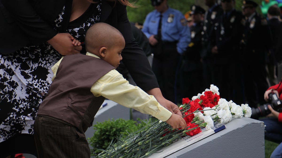 Three-year-old Robert Wilson IV accompanied by his mother, Crystal Faisson, places a white carnation beside his father's name at the Living Flame memorial at Franklin Square. (Emma Lee/WHYY)