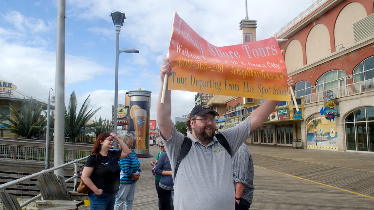 Levi Fox of Jersey Shore Tours holds up banner to gather people on the Atlantic City Boardwalk before giving a walking tour of the boardwalk.   (Anthony Smedile for NewsWorks)