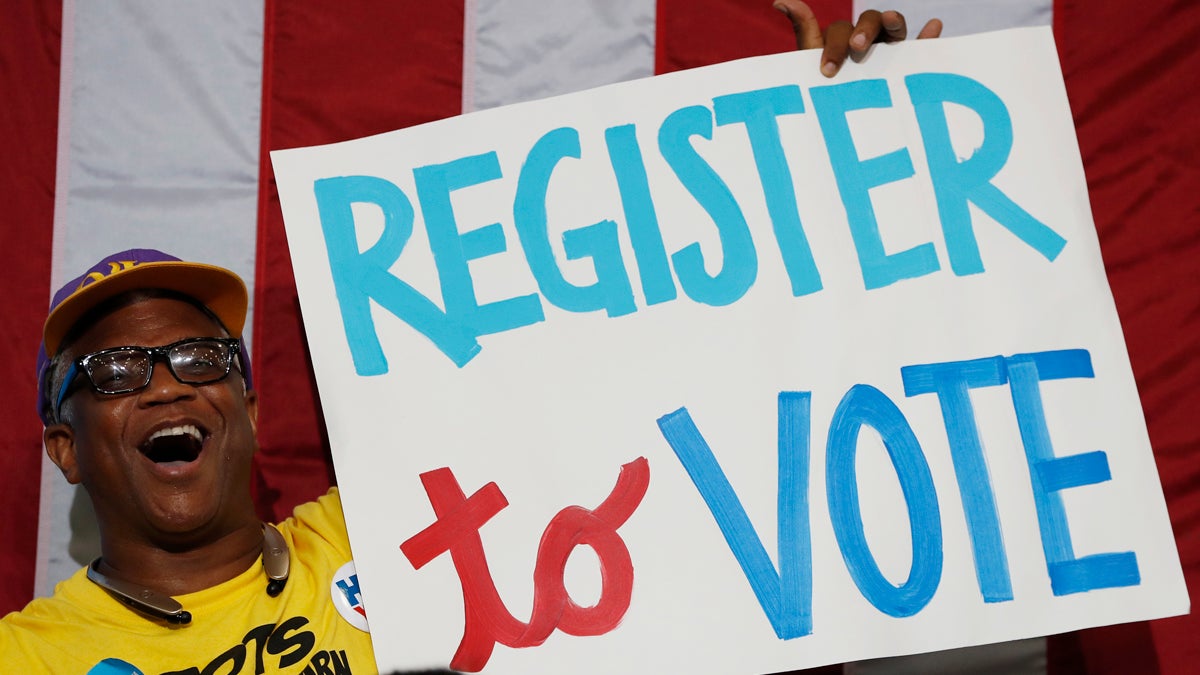 A man smiles while holding a sign that says, 