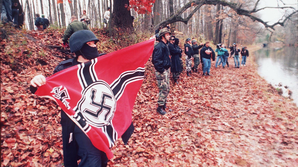  An unidentified member of a neo-Nazi group displays a Nazi battle flag by the Delaware Canal as others engage in a shouting match with opponents on the other side of the canal during an anti-gay rally last year in a state park in Washington Crossing, Pennsylvania. Both groups also hurled rocks, bottles, and sticks at one another as hundreds of state police stood by. (AP Photo/Widman) 