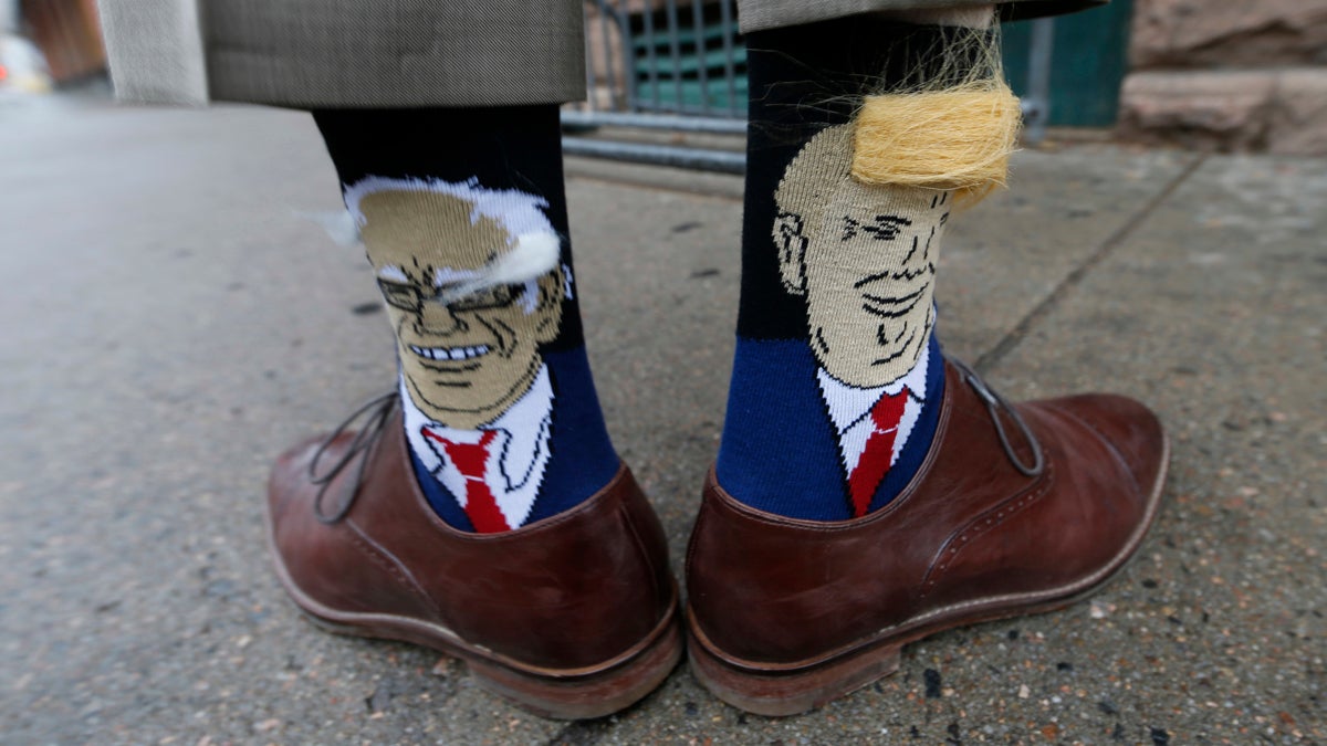 Colorado Gov. John Hickenlooper shows off his socks--one with Democratic presidential candidate Bernie Sanders and the other with Republican candidate Donald Trump--before entering his former brewpub for a book signing event to mark the release of his autobiography Thursday, May 26, 2016, in Denver. Hickenlooper, who is term-limited, is doing book talk rounds this week, reviving speculation that he is positioning himself to join Hillary Clinton's presidential campaign ticket. (AP Photo/David Zalubowski)