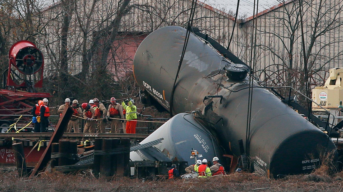 Workers secure lines around a train tank car as they prepare to pull it up with a crane from a crash site on a small bridge on the Mantua Creek
