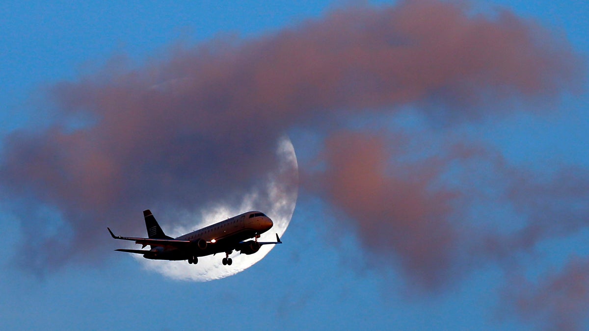 An airplane passes the moon as it makes its approach to Philadelphia International Airport
