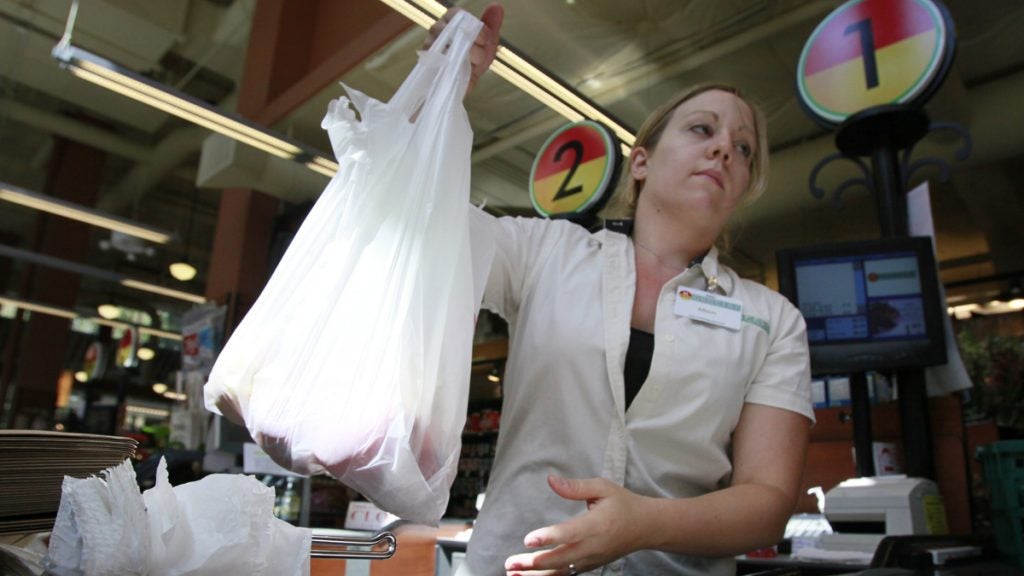 A cashier is pictured holding a plastic shopping bag with items inside.