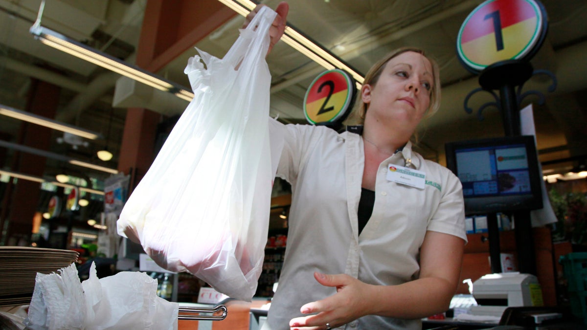A cashier is pictured holding a plastic shopping bag with items inside.
