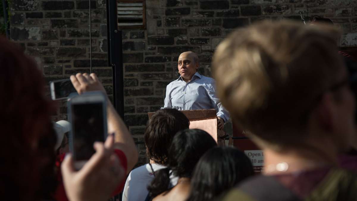 Vlad, portrayed by Jess Conda, addresses the crowd in the manner of a Sean Spicer White House press briefing