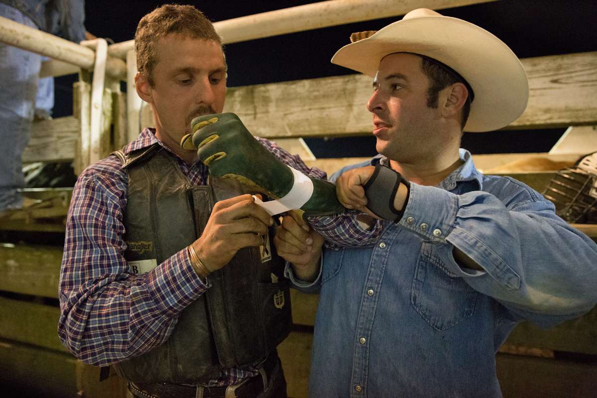 Bareback rider Jim Elchak helps bull rider Nat Brenize tape his gloves. (Lindsay Lazarski/WHYY)