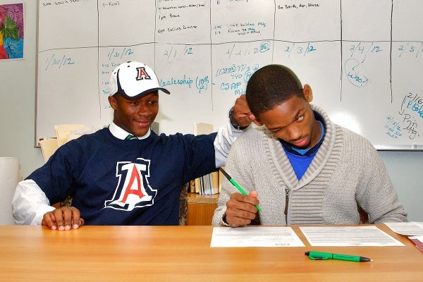 While signing his letter of intent to attend St. Francis University, Myles Brooker deals with an interruption from his friend since the age of six. (Bas Slabbers/for NewsWorks)