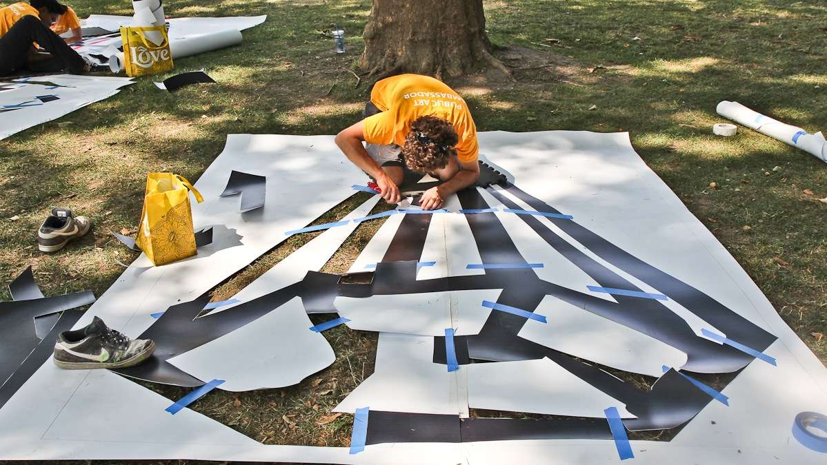 John Souter cuts out diamond stencils to paint around the edges of the lot. (Kimberly Paynter/WHYY)