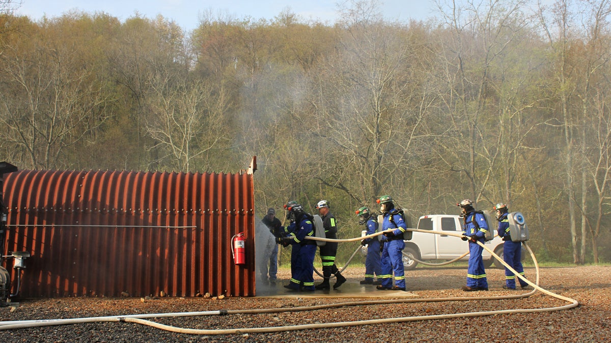  Members of the Mettiki Mine Rescue team prepared for one of the mine rescue competition’s timed events, the live burn: teams contain and then extinguish a fire in the hangar. They wear flame-resistant suits, fire-rated gloves, and breathing apparatuses. (Margaret J. Krauss/WESA) 