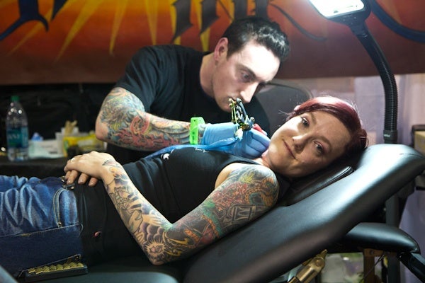 N.J. tattoo artist Jamie Schwartz receives a rose tattoo on her neck by fellow artist John Moscaritolo. (Kimberly Paynter/For NewsWorks)