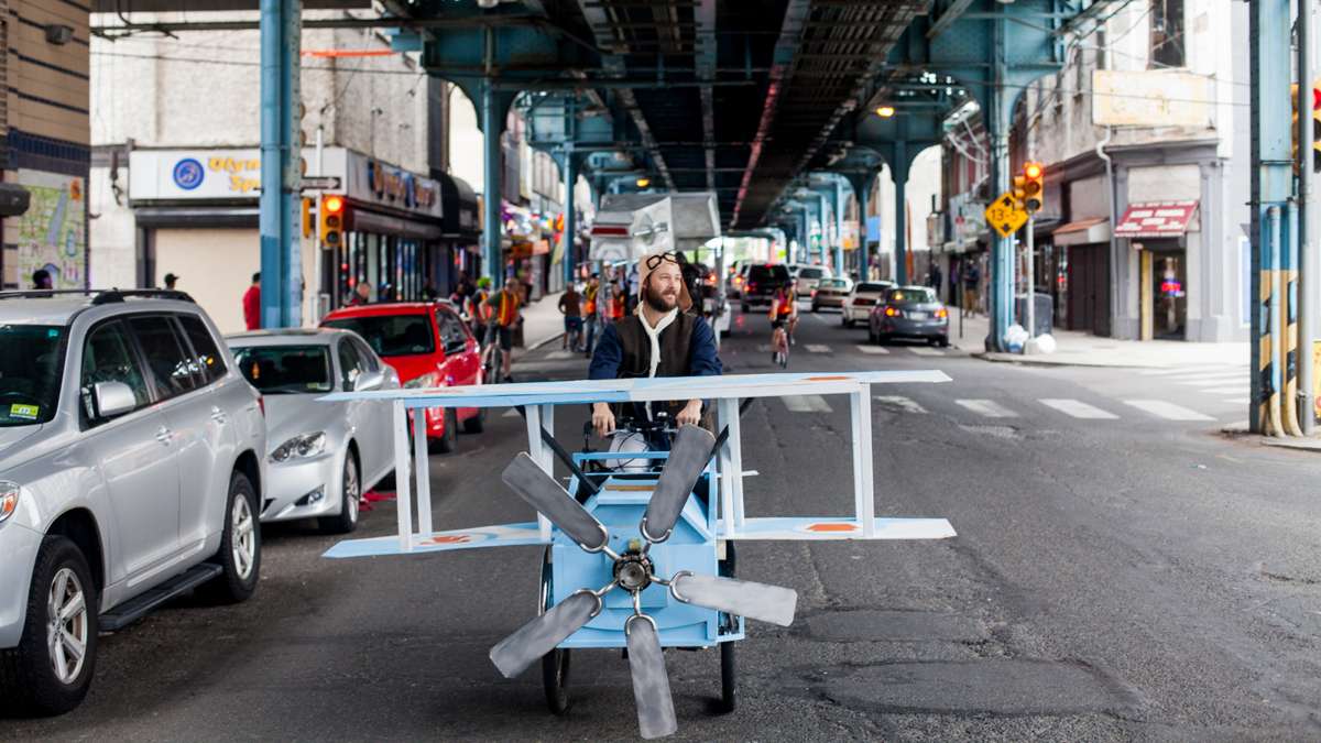 A man pilots a kenetic sculpture shaped like a biplane pedals down Front Street