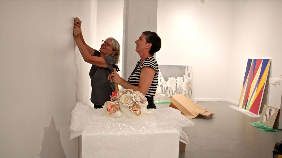 Jane Irish (left) and Mary Henderson of Tiger Strikes Asteroid galleries set up a show at the Crane Arts Building, their first since a fire displaced them from the Vox building on North 11th Street. (Emma Lee/WHYY)