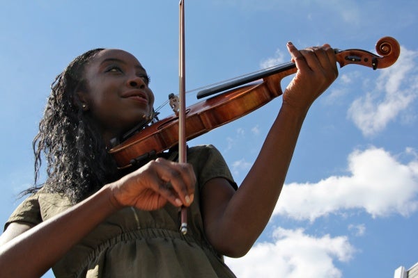 Gomian Konneh, 17, plays her violin in her East Oak Lane neighborhood. She is a senior at Masterman High School where extracurricular activities are on the chopping block.