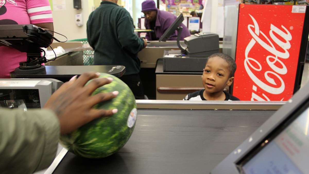 Tyrone Thomas, 5, shopping with his mother, Atoshia White, watches eagerly as his watermelon slides by the register. (Emma Lee/WHYY)