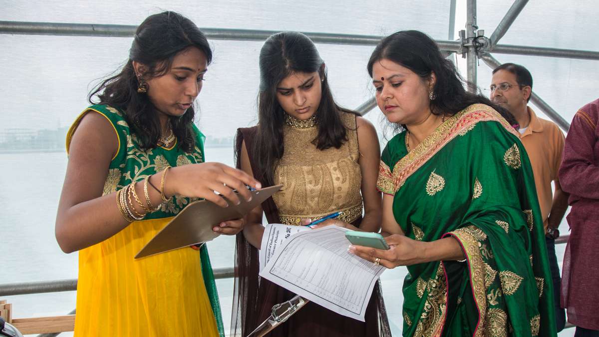 Manisha Jain, the cultural chairperson for the Festival of India (right), goes over the order of dance groups with emcees Priya Ganesh (far left) and Anika Sangal. (Emily Cohen for NewsWorks)