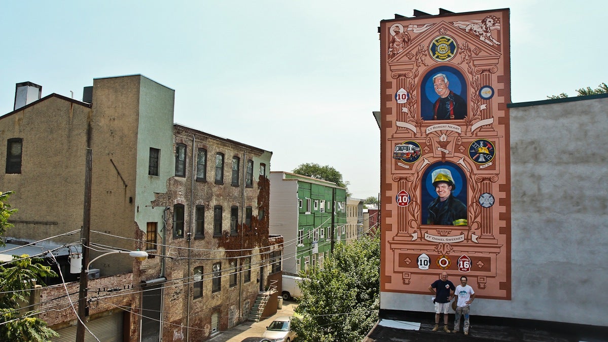 Artists Jesse Gardner and David McShane stand in front of a mural paying tribute to Lt. Robert Neary and firefighter Daniel Sweeny at 2024 Arizona Street in East Kensington. A fire that took place at York and Front streets a few blocks away claimed the lives of Sweeney and Neary in April of 2012. (Kimberly Paynter/WHYY) 
