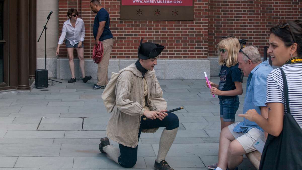 Matthew Skic, assistant curator of the event, explains the fife to museum goers outside of the Museum of the American Revolution Saturday. (Brad Larrison for NewsWorks)