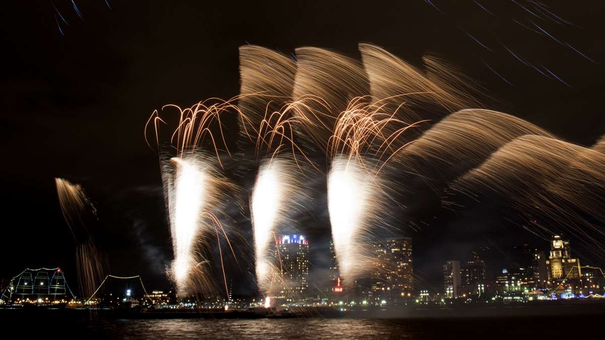 Fireworks explode over the Delaware River as seem from the Camden Waterfront with Penn's Landing and Society Hill in the background.
