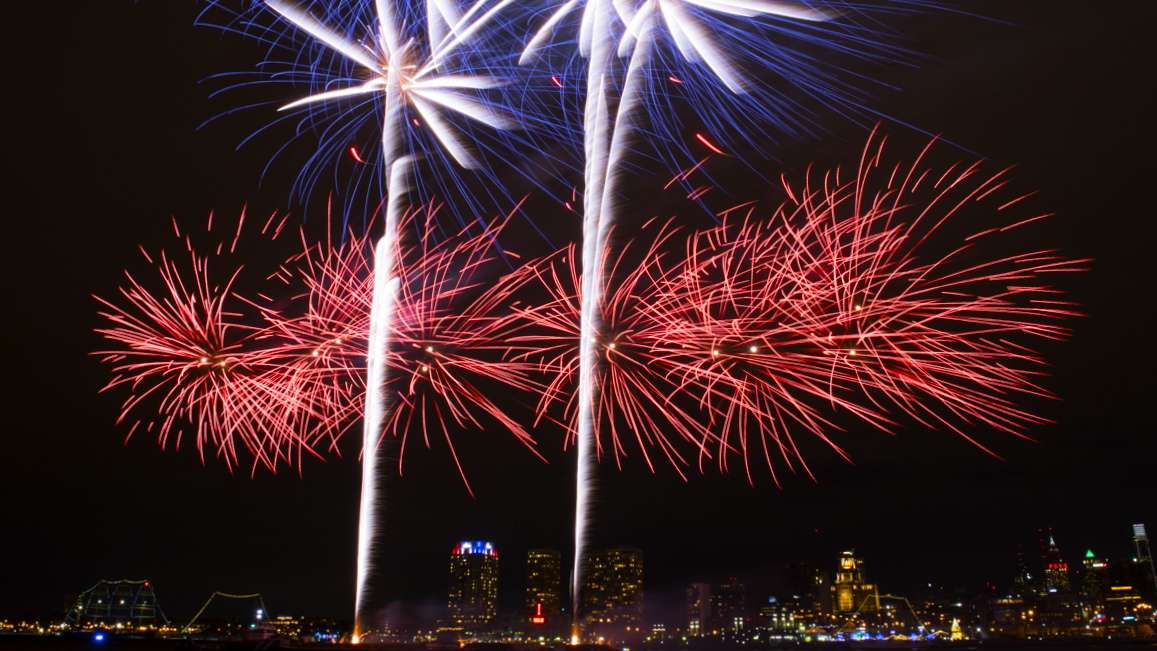 Fireworks explode over the Delaware River as seem from the Camden Waterfront with Penn's Landing and Society Hill in the background.