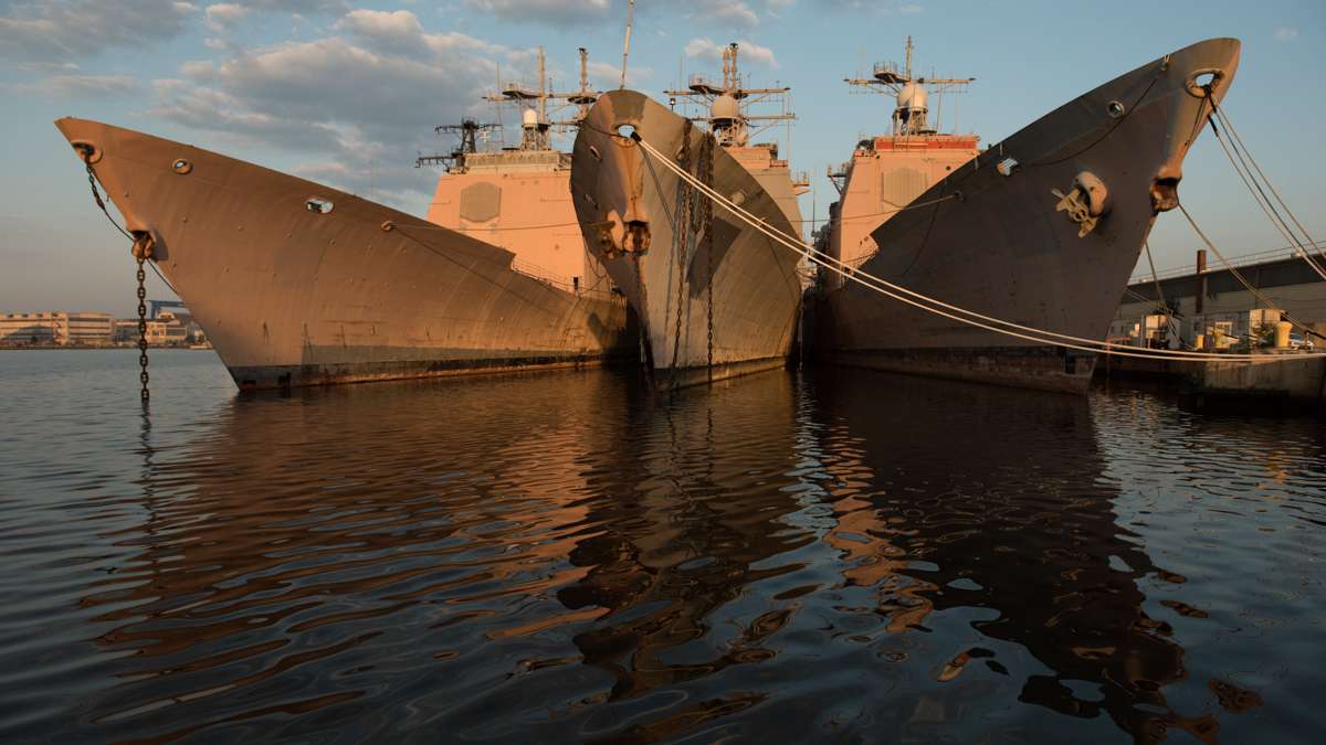 Three ships are reflected in the water at the Philadelphia Navy Yard.