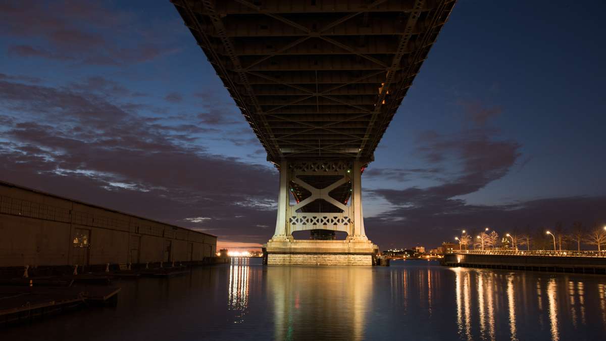 The underside of the Ben Franklin Bridge is silhouetted against the pre-dawn sky while the river reflects the still glowing street lights.