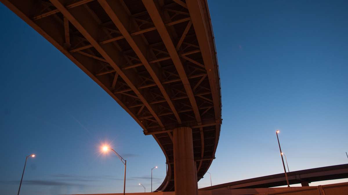 The sky glows blue with pre-dawn light as seen from beneath a highway overpass.