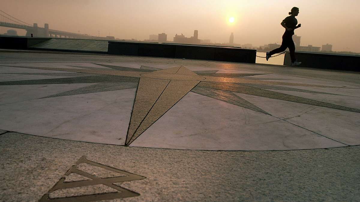 A woman jogs past a compass embeded in the floor of the amphitheater at Penns Landing as the sun rises over the Delaware River.