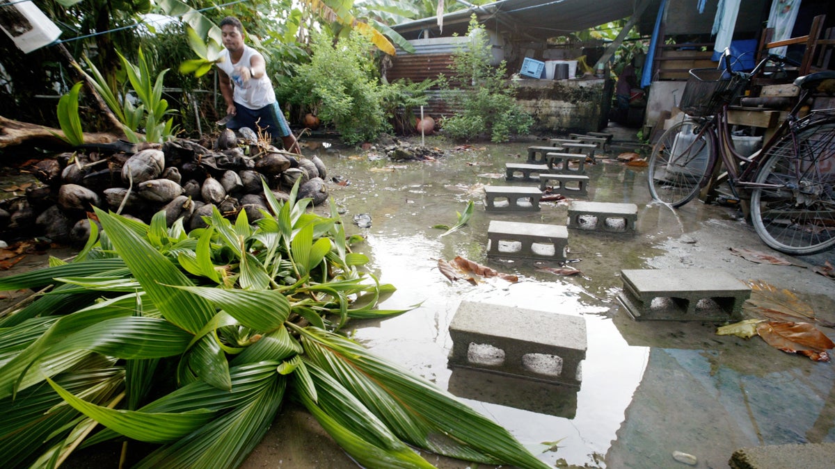  David Losia, 21, cuts coconuts for the family pigs in front of his family house flooded by the rising tides where cinder blocks are used as a makeshift walkway in Funafuti, Tuvalu. (AP Photo/Richard Vogel) 