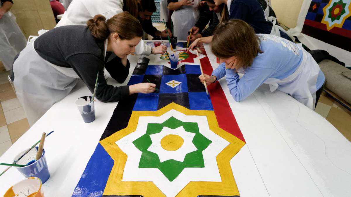 Community members help fill in the decorative elements of what will become parts of a banner along the building’s roof. (Bastiaan Slabbers/for NewsWorks)  