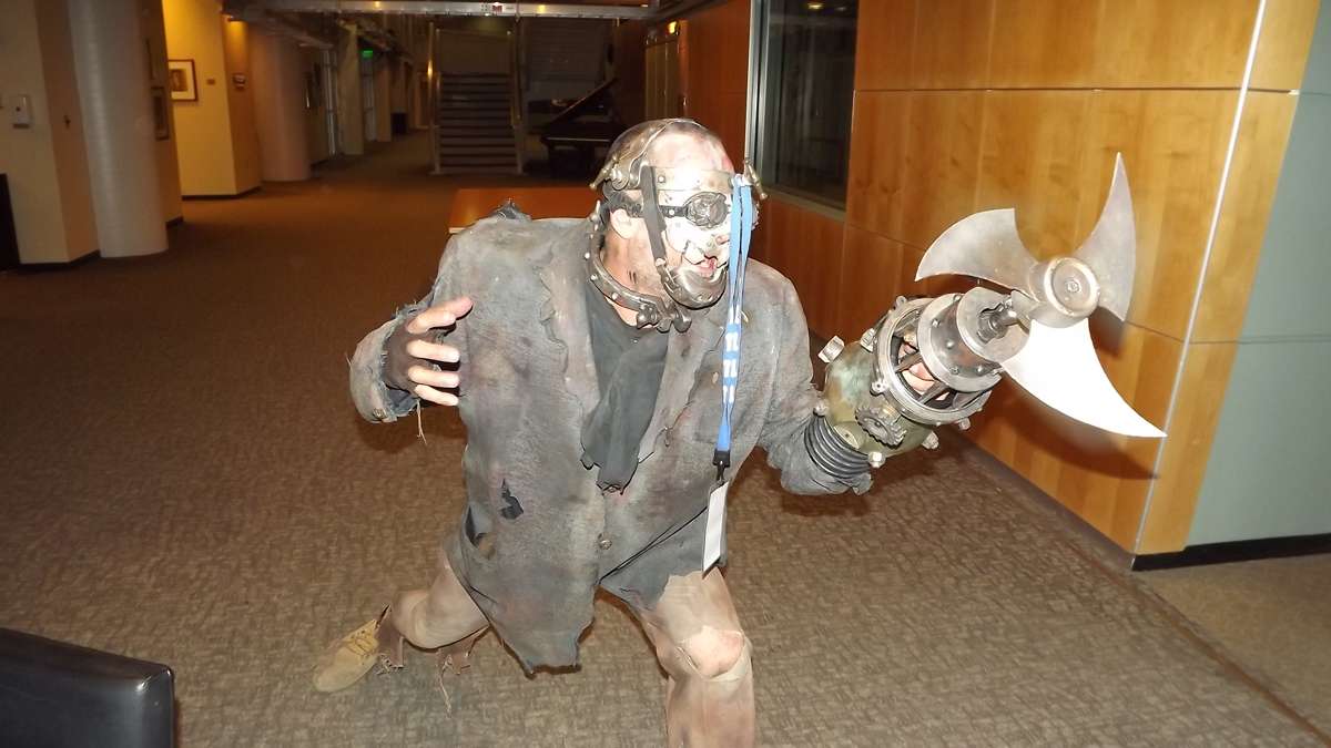 Scary zombie guy, dangling his visitor badge from a knob on his head, twirls his blade and strikes a pose at WHYY studios. (Jeanette Woods/WHYY)
