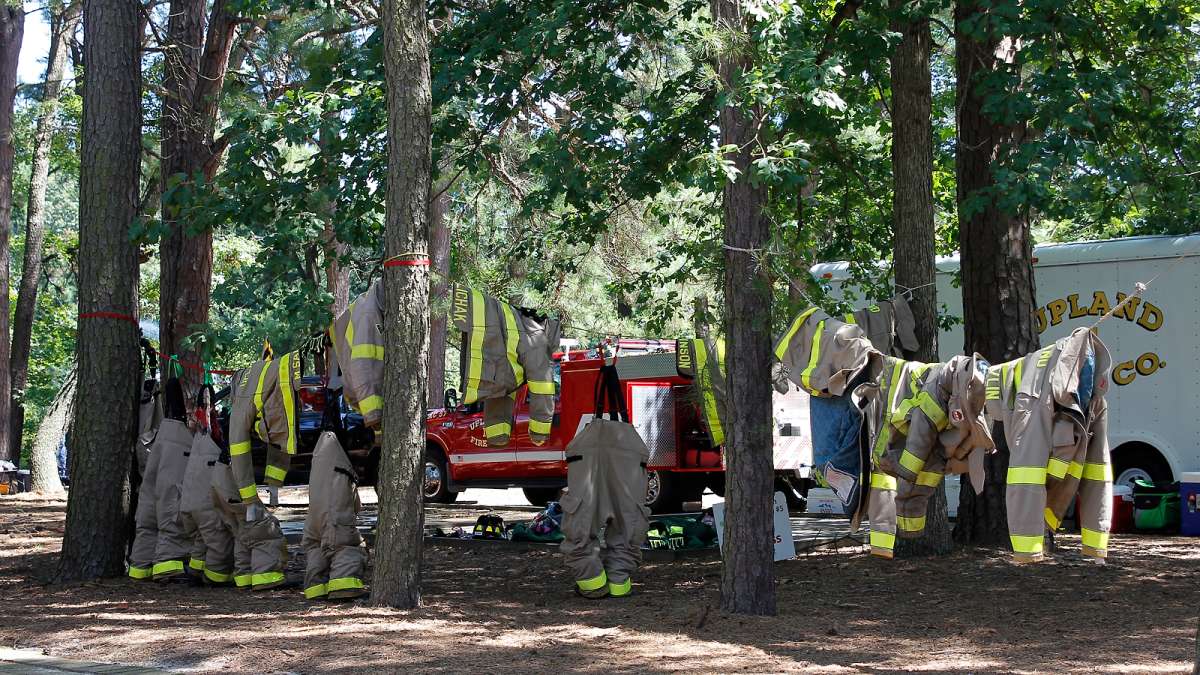 Fire fighters' protective suits hang in a shady grove at the 37th Annual Fire Apparatus Show and Muster at WheatonArts, in Millville, NJ, on Sunday. (Jana Shea for NewsWorks)