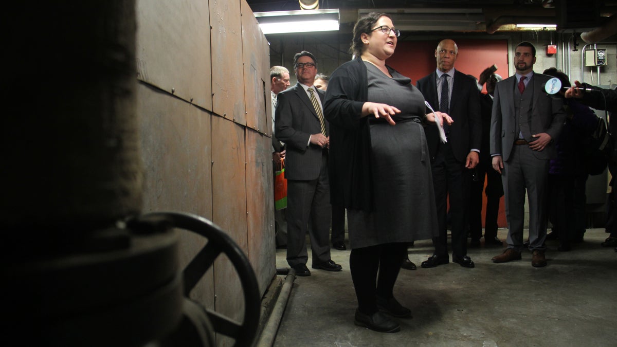  Emily Schapira, executive director of the Philadelphia Energy Authority, talks to reporters in front of an old boiler in the basement of Lankenau High School, an example of the kinds of improvements that could be made under the Energy Pilot Project. (Emma Lee/WHYY) 