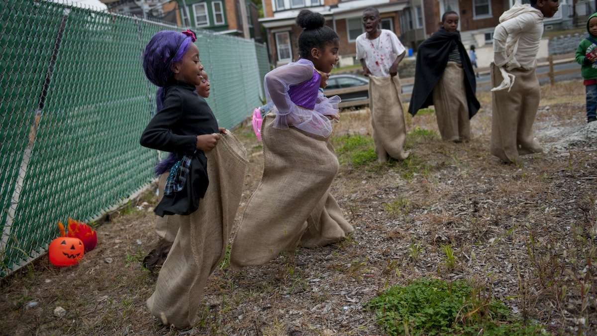 Cymaiah Marc (left), 6, and Makayla Oduardo (center), 6, participate in a potato sack race during the West Rockland Street Halloween Party in Germantown on Halloween evening. (Tracie Van Auken/for NewsWorks)