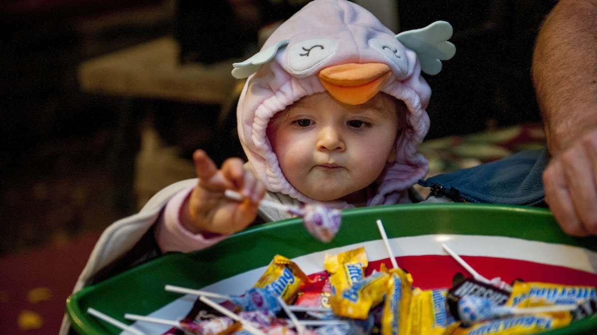 Evie Valiante, 18 months, takes a lollipop from Jim McCafferty in Chestnut Hill on Halloween night. (Tracie Van Auken/for NewsWorks)