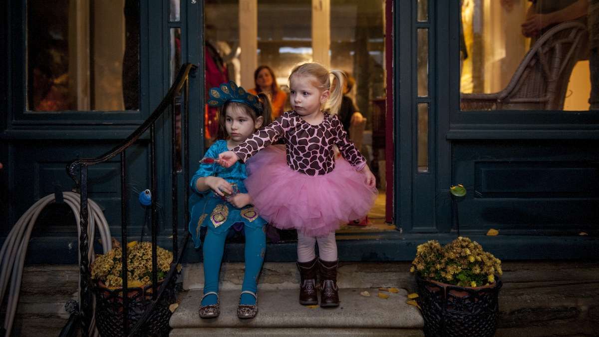 Ava Sylvester, 2, and her sister, Audrey, 4, stand on their front porch in Chestnut Hill and wait to give candy to trick-or-treaters on Halloween night. (Tracie Van Auken/for NewsWorks)