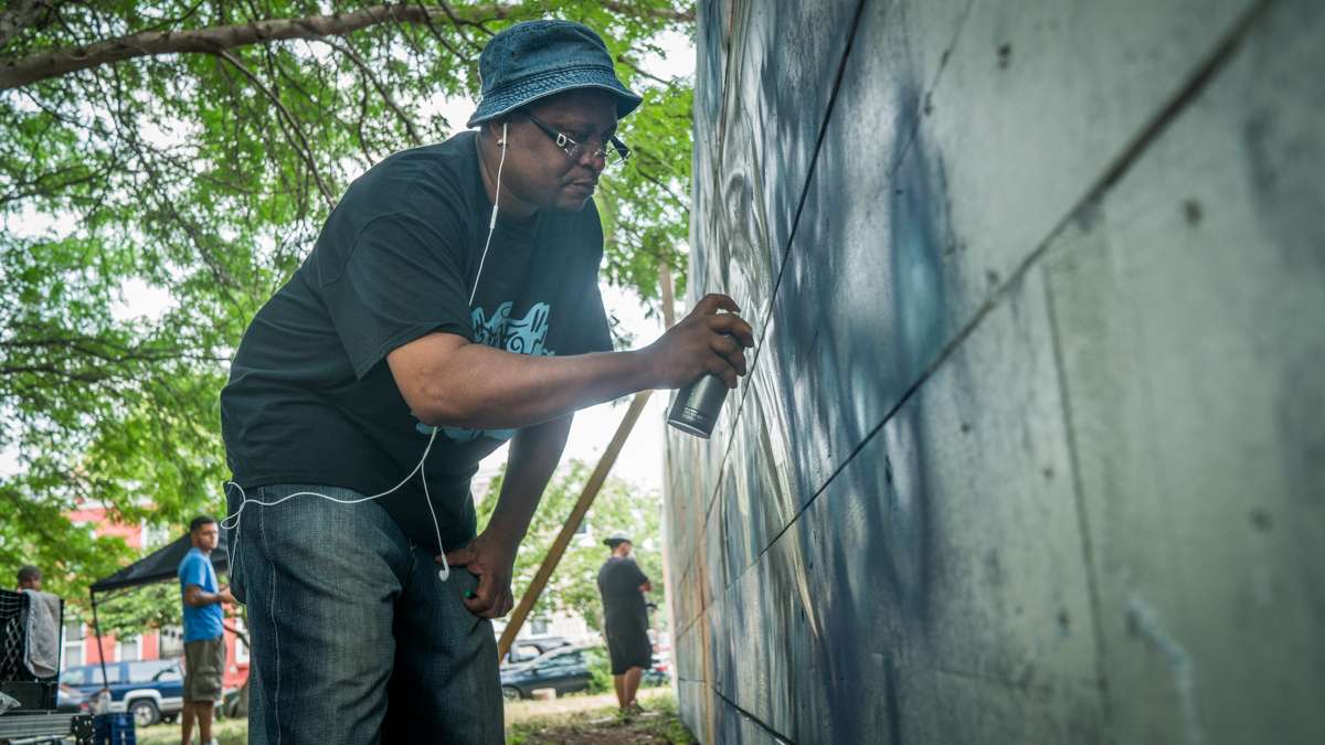 A graffiti writer paints on a wall