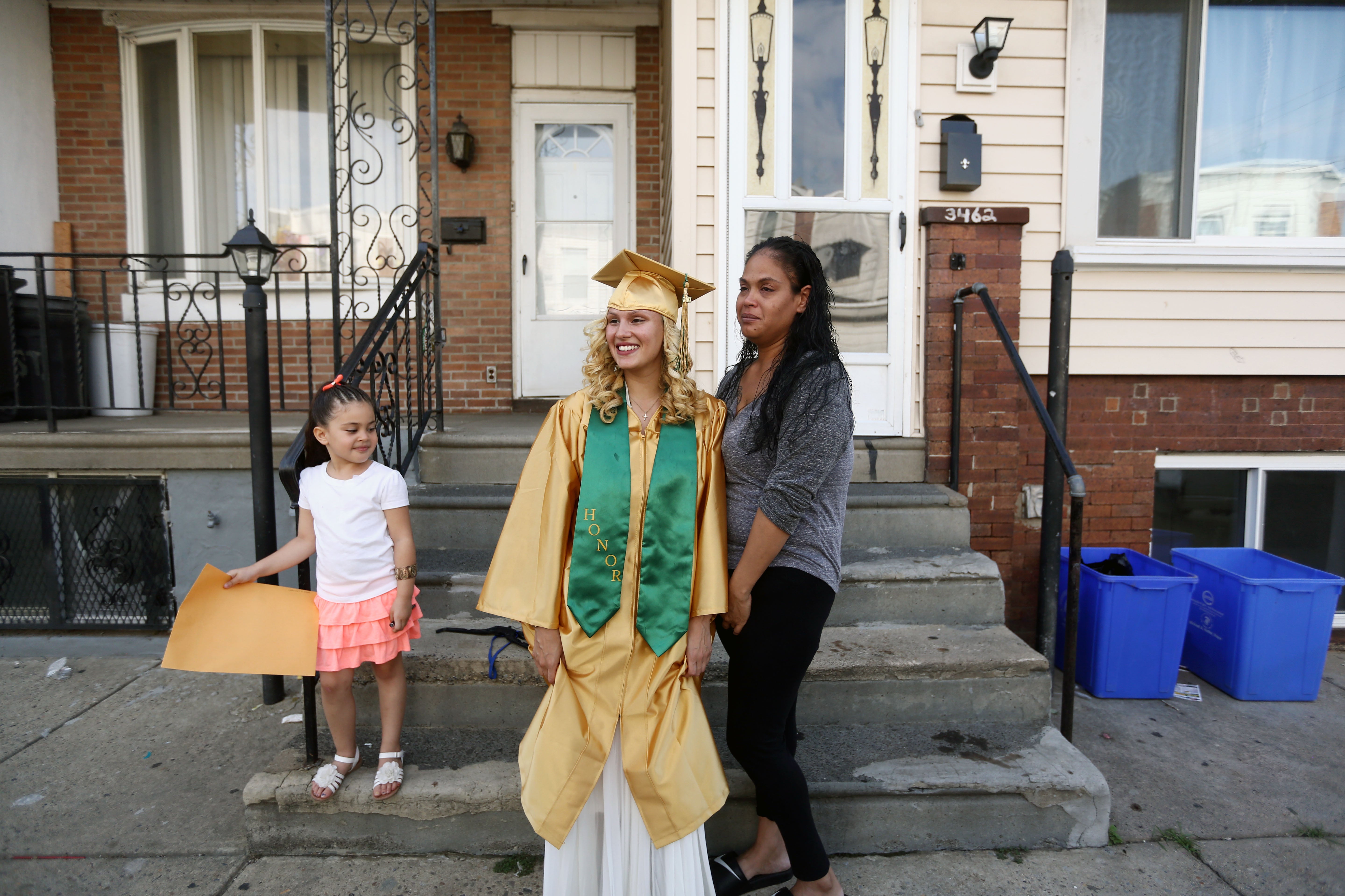 Savannah and Neverlyn pose for pictures outside of their home in Kensington on graduation day as Layla looks on. (Jessica Kourkounis/For Keystone Crossroads)