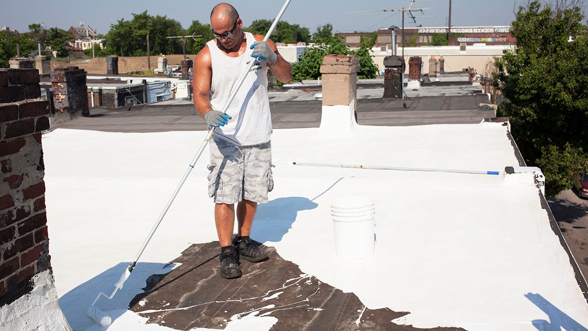 Roofer Rob Nolfi applies a reflective topping on a rehabbed roof in North Philadelphia. Cool roofs help keep temperatures down when the city heats up. (Irina Zhorov/The Pulse)