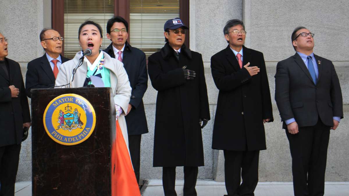 Ji Hyun Choe of the Society of Young Korean Americans sings the Republic of Korea National Anthem as the Korean flag is raised outside City Hall in recognition of Korean American Day.