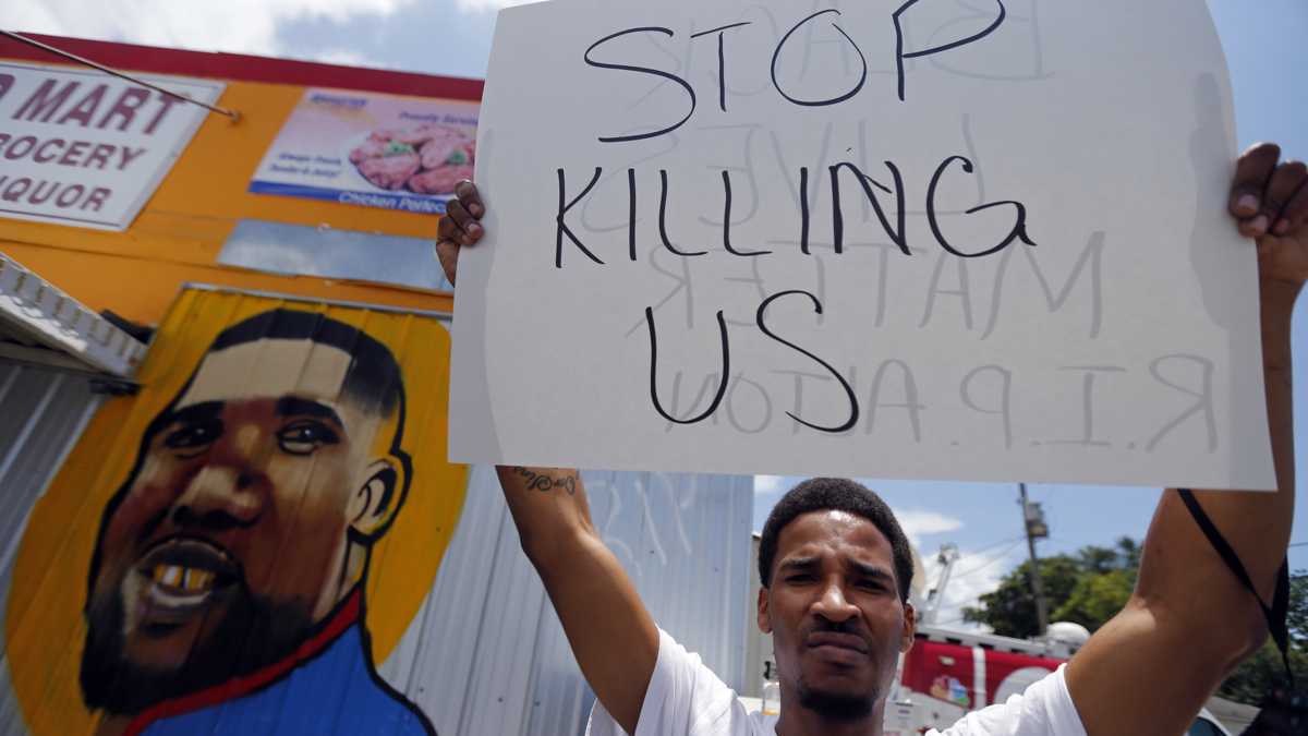  A man holds a sign in front of a mural of Alton Sterling while attorneys, not pictured, speak in front of the Triple S Food Mart in Baton Rouge, La., Thursday, July 7, 2016. Sterling, 37, was shot and killed outside the convenience store by Baton Rouge police, where he was selling CDs. (AP Photo/Gerald Herbert) 