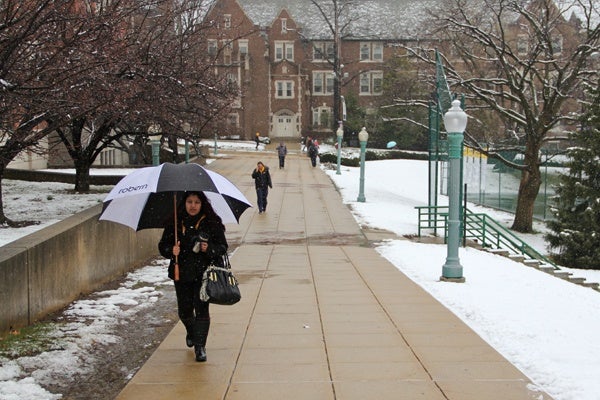 A woman with an umbrella walks through the snow-covered La Salle campus.
